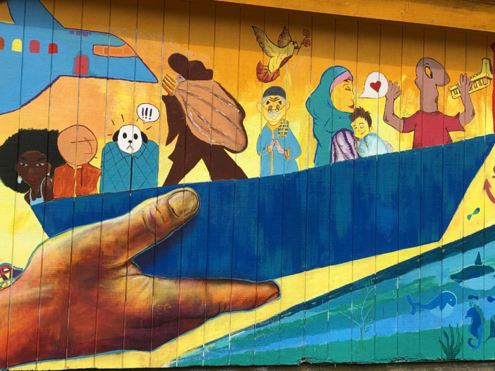 Boldly colored mural featuring diverse people in a boat together. Mural is at the Vassar College Farm and Ecological Preserve, Poughkeepsie, NY
